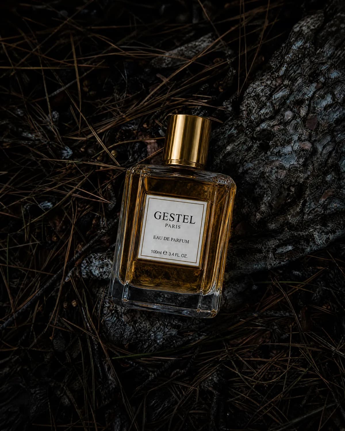 GESTEL perfume bottle on dark bark, pine needles, and moody natural texture.