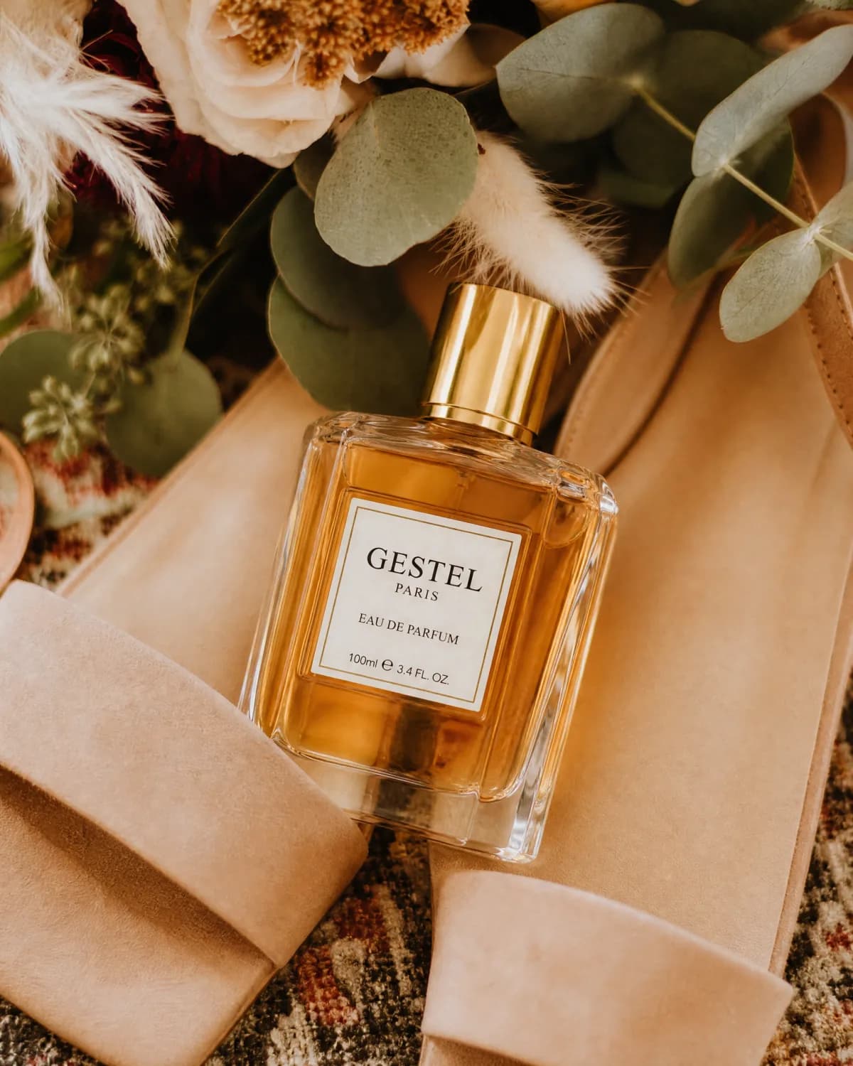 GESTEL perfume bottle styled with warm leather, soft florals, and eucalyptus leaves.